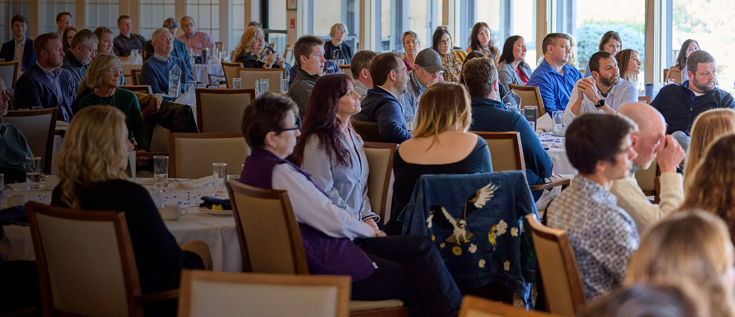people in business clothes at a conference sitting at tables and listenting to a speaker